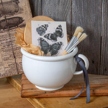 Load image into Gallery viewer, ironstone chamber pot vignette with wooden board, paint brushes, and butterfly illustration