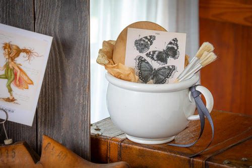 ironstone chamber pot vignette with wooden board, paint brushes, and butterfly illustration
